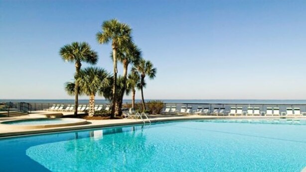 A clear blue pool with palm trees and lounge chairs.