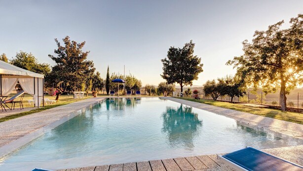 Piscina retangular com deck de pedra, espreguiçadeiras e área coberta com mesa e cadeiras.