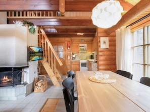 Un interior de madera con chimenea, mesa de comedor y zona de cocina.