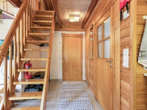 Un escalier en bois menant à une porte, un extincteur posé sur le sol et un tapis à motifs.