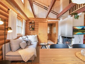 Ein gemütliches Blockhaus-Interieur mit Holzbalkendecke, einer Couch mit Kissen, einem kleinen runden Tisch und einem Kamin.