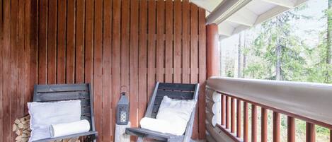 A wooden deck with two chairs, a lantern, and a railing.