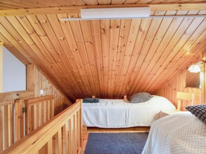Eine Holzhütte mit Schlafzimmer im oberen Bereich, einem kleinen Tisch und einer Bank.