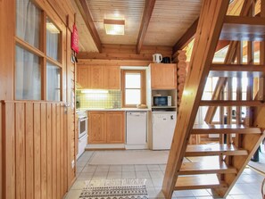 A wooden interior with a kitchen, a refrigerator, a microwave, and a wooden staircase.
