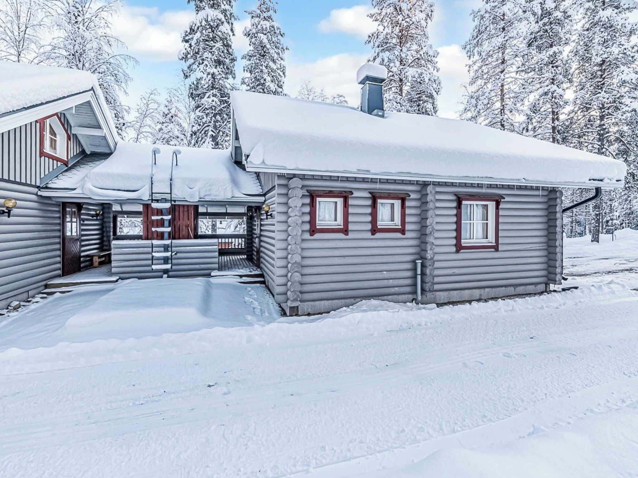 Une cabane en rondins avec un toit enneigé et une véranda en bois.