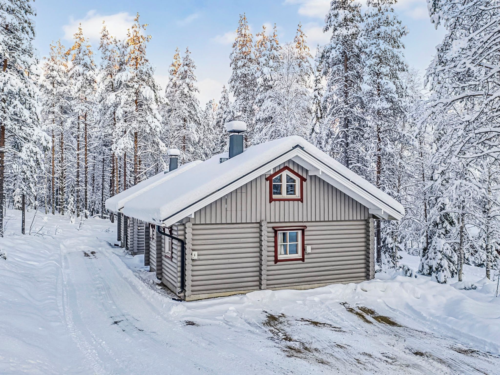 A log cabin with a gabled roof, surrounded by a snowy forest.