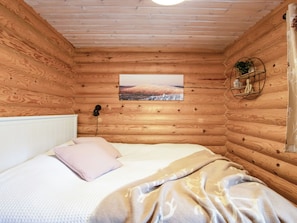 Habitación de cabaña de madera con una cama, un cuadro en la pared y un estante circular con una planta.