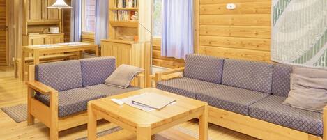L’intérieur d’un chalet accueillant, avec une table à manger en bois, deux canapés, une bibliothèque et une fenêtre avec des rideaux.