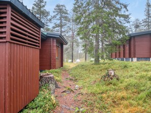 A row of cabins with a forested backdrop, a gravel path, and a clear sky.