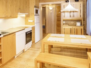Eine kleine Küche mit weißen Geräten, Holzschränken und einem Essbereich mit Tisch und Bänken.