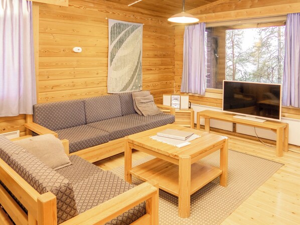 A cozy wooden cabin interior with a sofa, a coffee table, a television, and a large window.