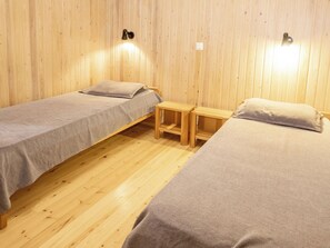 Ein Zimmer mit zwei Einzelbetten, Holzboden und einem kleinen Holztisch dazwischen.