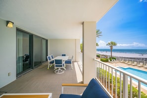 Un balcón con piscina, un comedor con sillas y vista a la playa.