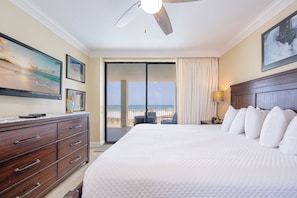 Quarto de hotel com uma cama grande, ventoinha no teto, televisão e vista para a praia.