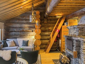 A cozy log cabin interior with a stone fireplace, a wooden ceiling, and a sofa with cushions. - Kelotorppa a by Interhome (Kuusamo)