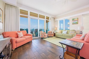A spacious living room with a large window, a wooden floor, and a view of the city.