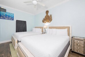 Une chambre d’hôtel avec deux lits, un ventilateur de plafond, une œuvre d’art accrochée au mur et une valise posée sur une commode.