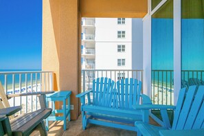 Un balcón con sillas Adirondack azules, una mesa pequeña y vistas a la playa y al océano.