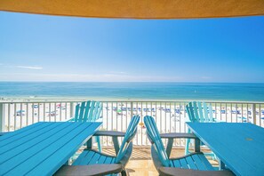 Une vue sur la plage depuis un espace abrité, équipé de tables et de chaises, donnant sur une plage de sable où se trouvent des parasols et des personnes.