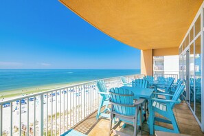 A balcony with a view of the beach and ocean, featuring a table and chairs.