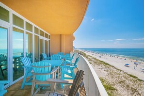 Uma varanda com cadeiras Adirondack azuis, uma porta de vidro que dá para a praia, e um céu claro.