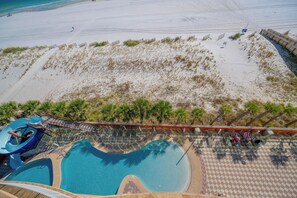 Zona de piscina con tobogán de agua y una playa al fondo.