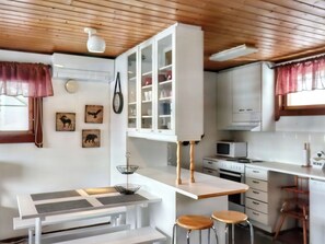 A modern kitchen with white cabinets, a microwave, and a dining area with stools. - Pieni kiiruna by Interhome (Hyrynsalmi)