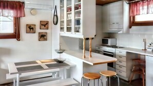 A compact kitchen with white cabinetry, a microwave, and a sink. There are two stools and a small table with a metal tray.