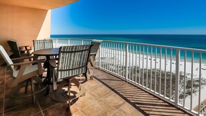 Un balcone con vista sulla spiaggia, un tavolo, sedie e una ringhiera.