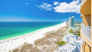 Una playa con cielo despejado, una orilla arenosa y un edificio alto con balcones que dan al mar.
