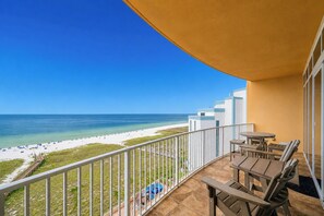 Un balcón con vista a la playa y el océano, muebles de madera y barandilla blanca.