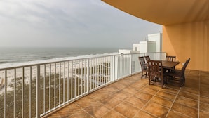 Un balcon donnant sur la plage et l’océan, une table avec des chaises et une balustrade blanche.