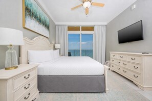 Une chambre d’hôtel avec un lit, une télévision, un ventilateur de plafond, un tableau et un balcon avec vue.