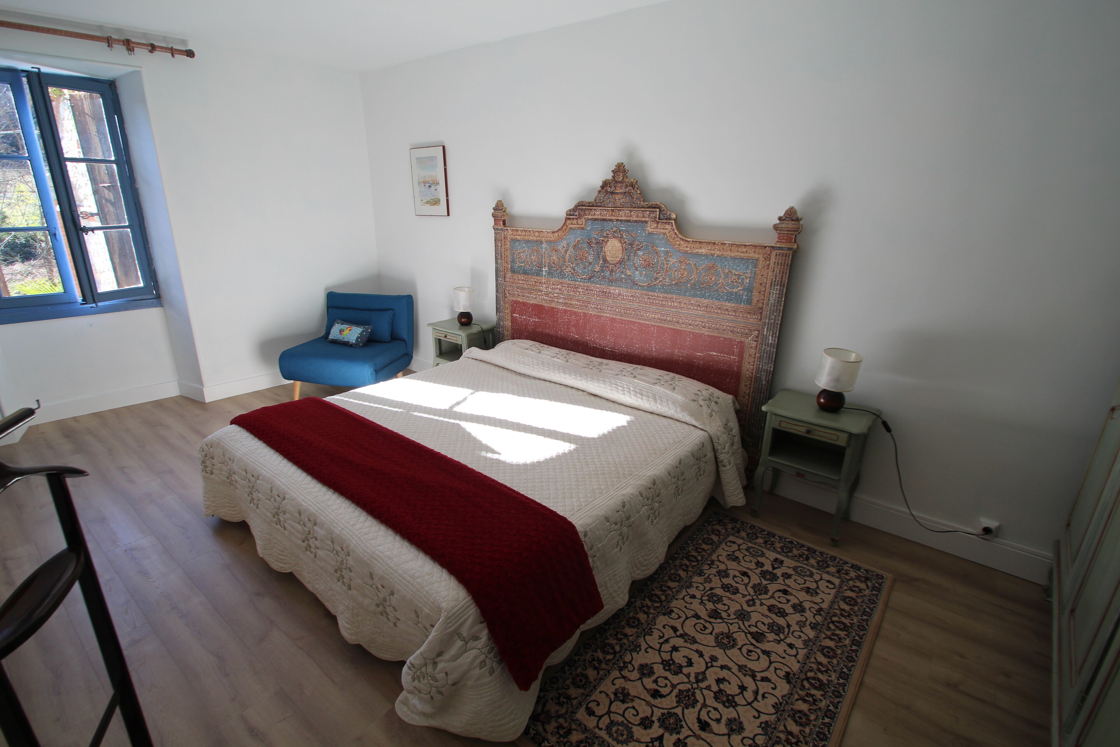 Een slaapkamer met een groot bed, een stoel, een nachtkastje, een lamp en een raam.
