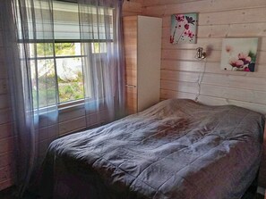 A bedroom with a bed, a window with curtains, a wardrobe, and two wall-mounted paintings.