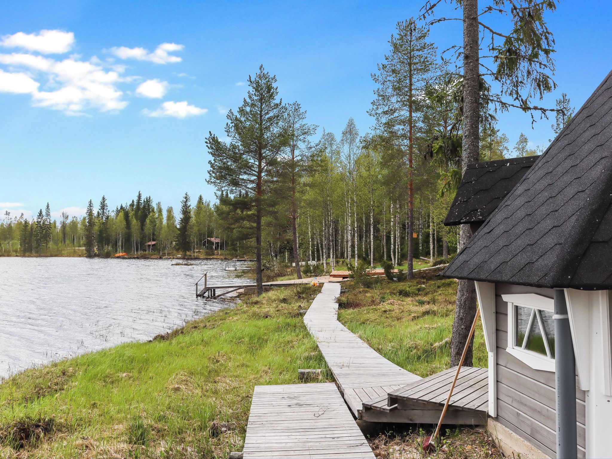 Une jetée en bois menant à un petit chalet situé au bord d’un lac, entouré d’arbres.