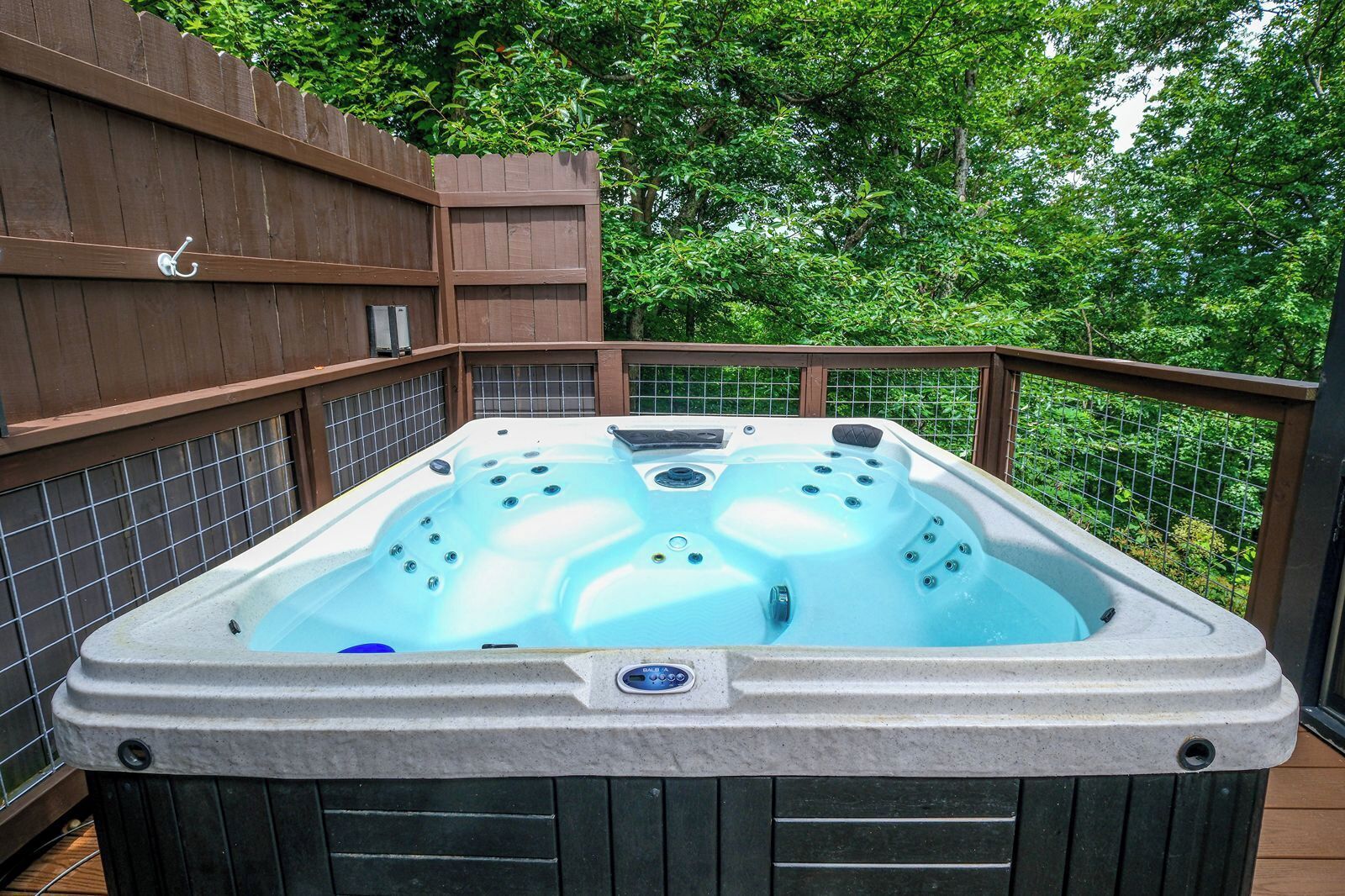 A hot tub on a balcony with a wooden fence and greenery in the background.
