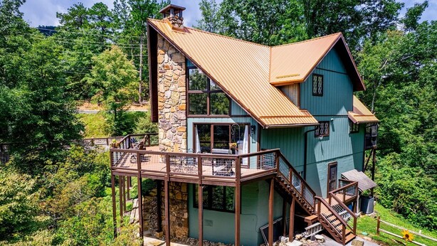 Ein zweistöckiges Haus mit Steinunterbau, einer Holzterrasse und einem Metalldach.