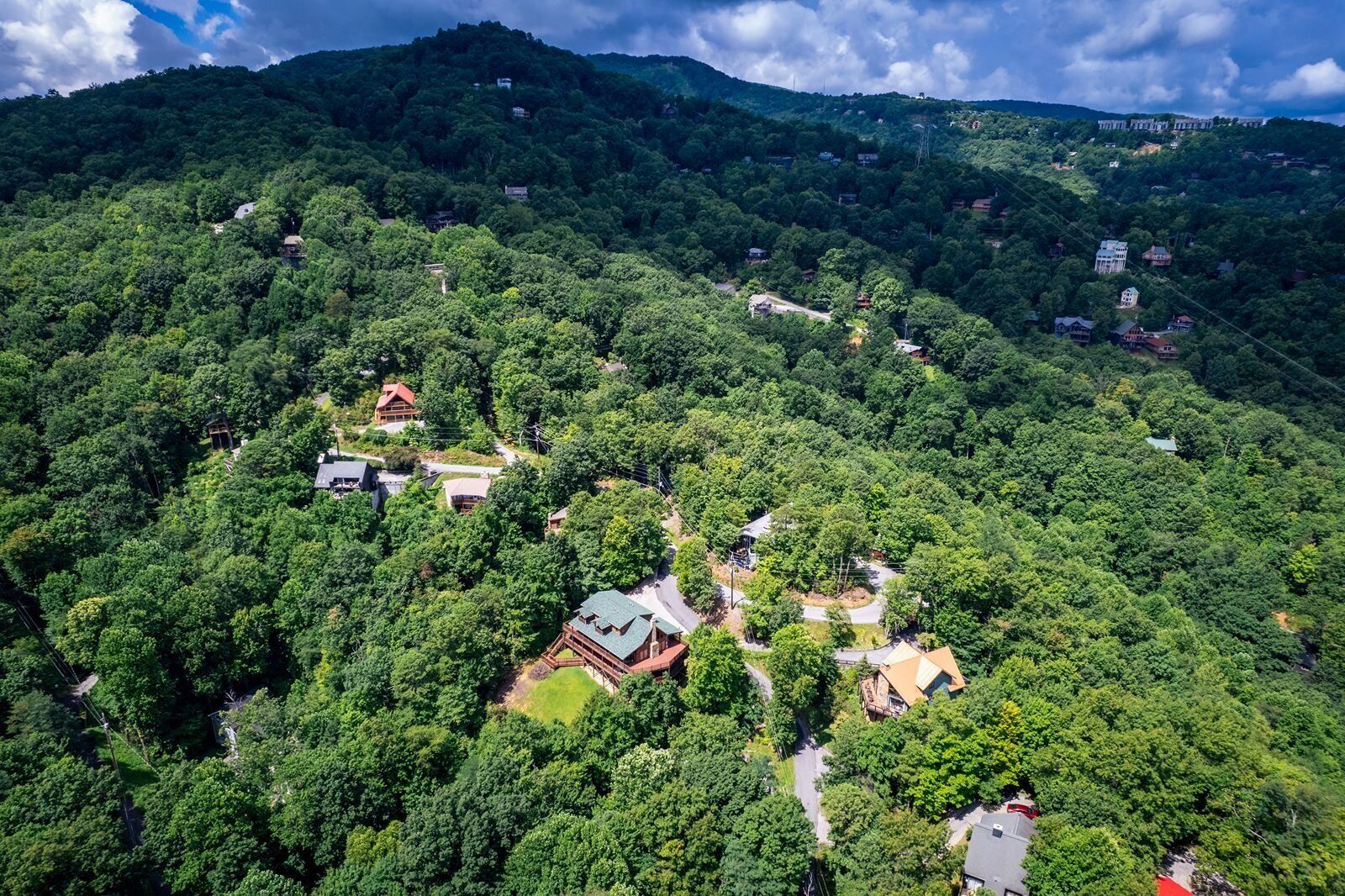 An aerial view of a mountainous area with scattered houses surrounded by dense forest.