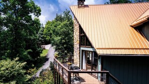 Ein Haus mit einer Holzterrasse und einem Steinkamin, umgeben von üppigem Grün.