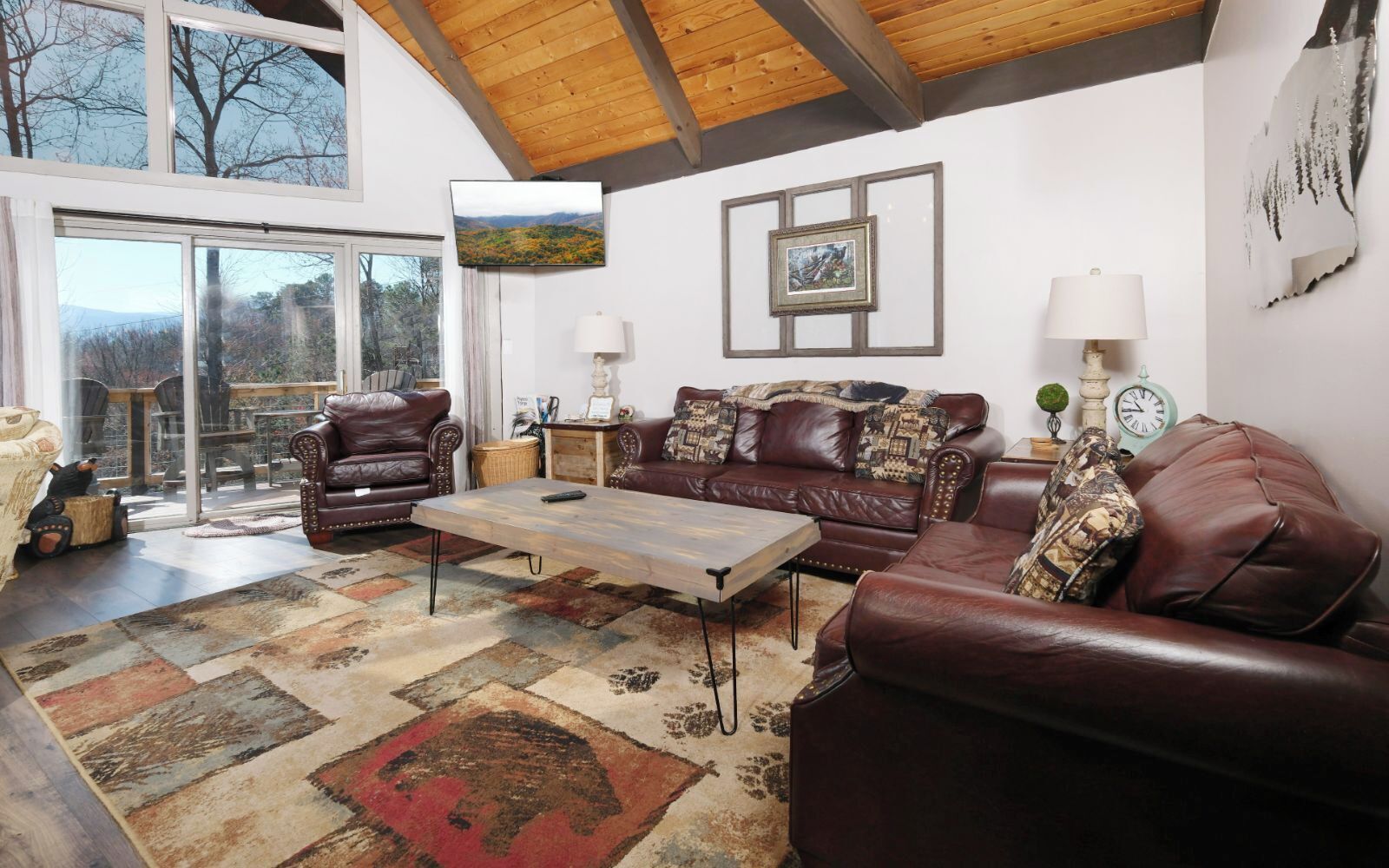 A spacious living room with a large window, leather sofas, a coffee table, and a patterned rug.