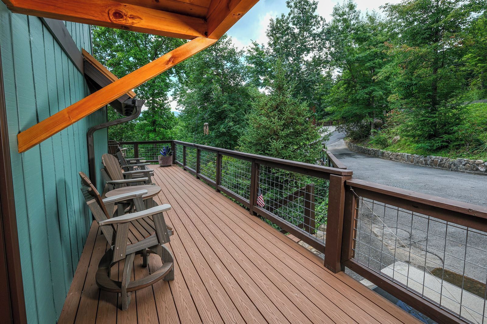 A wooden deck with picnic tables and a railing overlooking a road and greenery.
