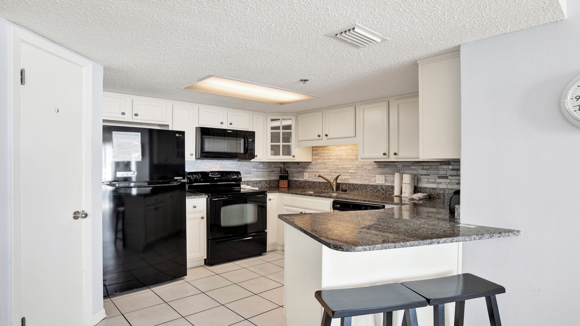 A modern kitchen with white cabinets, a black refrigerator, a microwave, a stove, and a granite countertop.