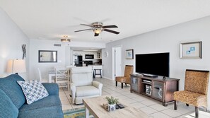 A modern living room with a sofa, chairs, a coffee table, a TV, and a ceiling fan.