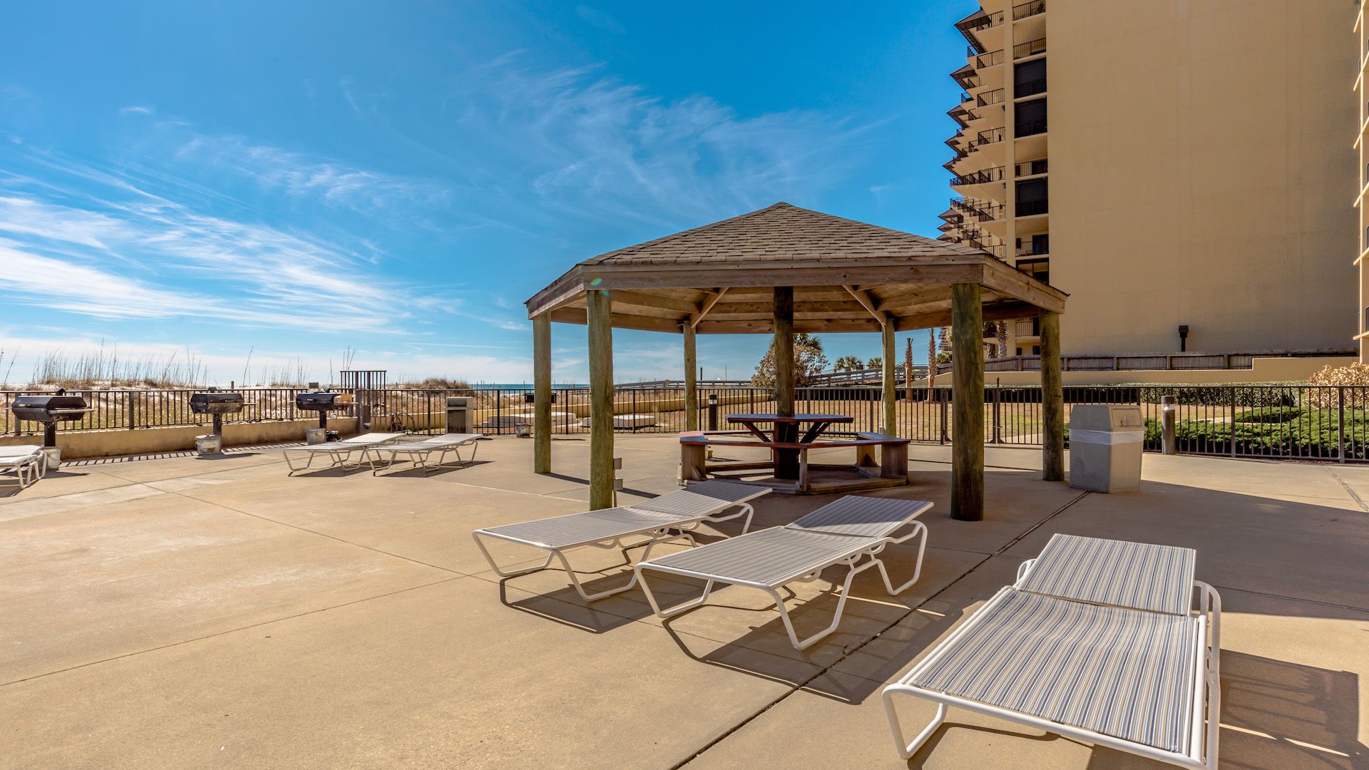 Une terrasse extérieure dotée d’un gazebo en bois, de chaises longues et de barbecues.