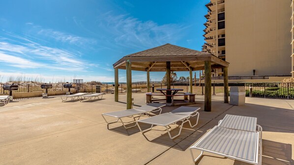 An outdoor patio with a wooden gazebo, lounge chairs, and barbecue grills.