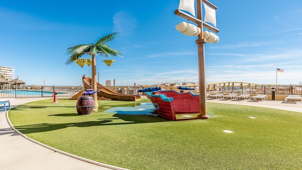 A playground with a slide, a ship-themed play structure, and palm trees.