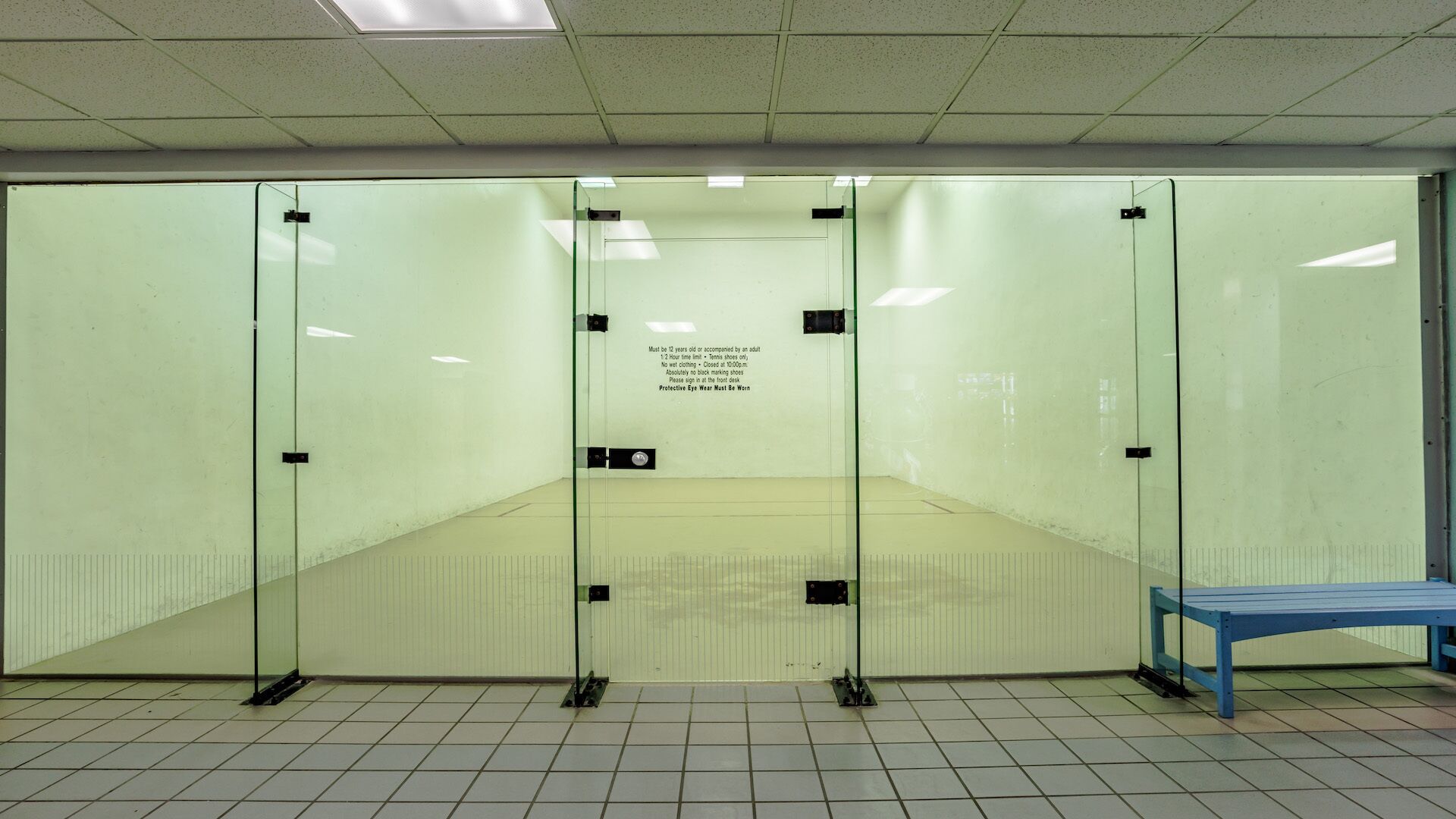 A glass-walled room with a bench, a sign with rules, and a tiled floor.