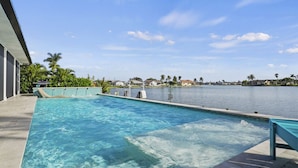 Una piscina con vista despejada al agua, un muelle y un lago tranquilo con casas al fondo.