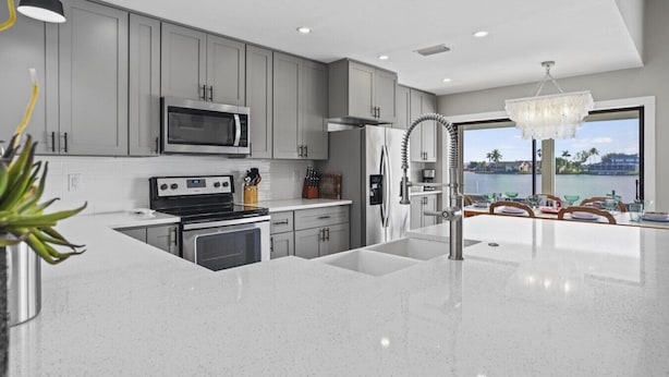 Una cocina moderna con gabinetes grises, electrodomésticos de acero inoxidable, una isla grande con un lavamanos y vistas a un lago a través de la ventana.